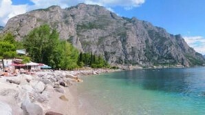 A beach with rocky shore, clear water, and a mountain in the background. - Hotel Sole - Limone (Limone sul Garda)