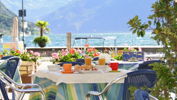 A table set with breakfast items, a view of the sea, and mountains in the background. - Hotel Sole - Limone (Limone sul Garda)