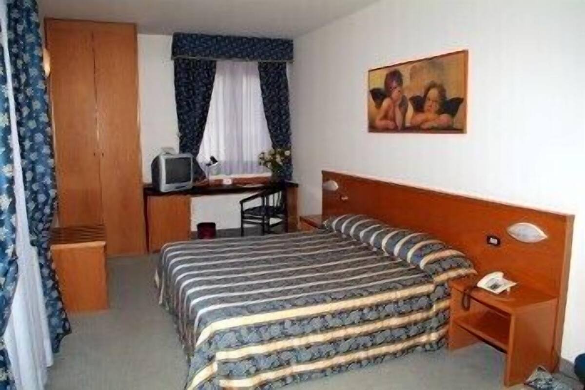 A hotel room with a bed, a desk with a television, a chair, and a painting on the wall.