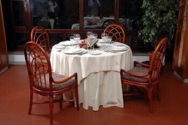 Una mesa redonda de comedor con mantel blanco, rodeada por cuatro sillas de madera con asientos acolchados.