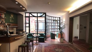 A hotel lobby with a bar area, seating, a large rug, and a view through a partition. - Le Mura (Città di Castello)