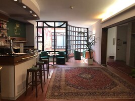 Un hall de hotel con una zona de bar, asientos, un tapete grande y una vista a través de una partición.
