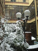 Un patio cubierto de nieve, con un farol y un edificio con grandes ventanales y balcones.