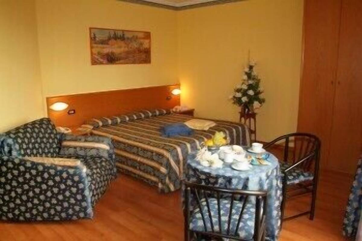 A cozy room with a bed, a chair, a small table with cups and a vase of flowers.