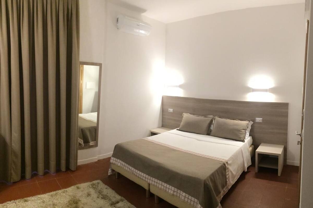 A hotel room with a bed, bedside tables, a mirror, and curtains.