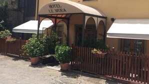 A hotel named "HOTEL LE MURA" with a covered outdoor seating area, potted plants, and a wooden fence. - Le Mura (Città di Castello)