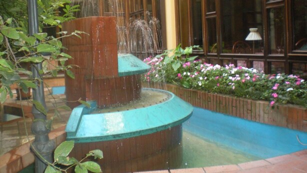 A fountain with water jets in a courtyard with a brick floor and flower beds. - Le Mura (Città di Castello)