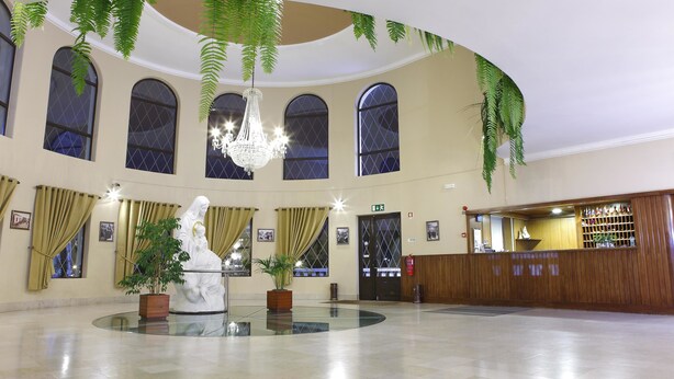 A lobby with a central statue, large windows, a reception desk, and hanging plants. - Domus Pacis Fatima Hotel (Ourem)