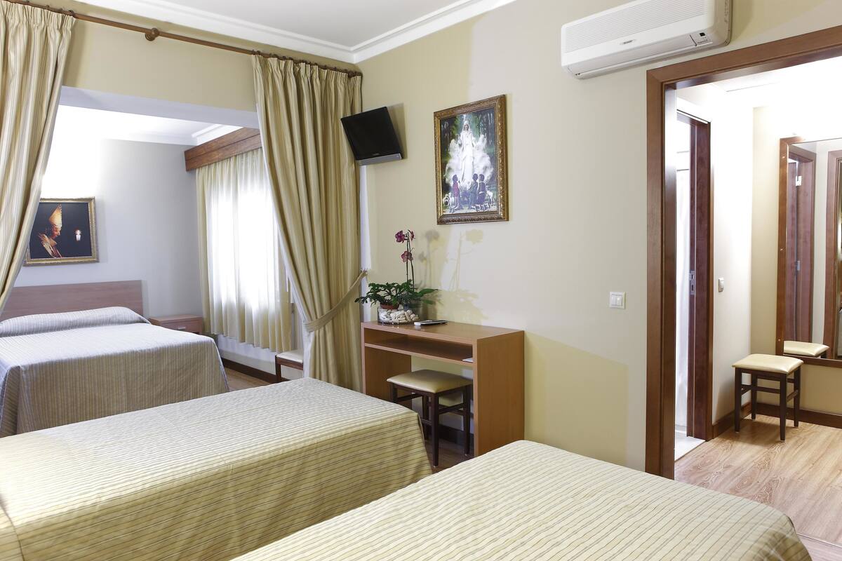 Habitación de hotel con dos camas, un escritorio, una silla, un televisor y un cuadro en la pared.