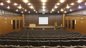 A large auditorium with rows of seats, a stage with a projector screen, and wooden paneling on the walls and ceiling. - Domus Pacis Fatima Hotel (Ourem)