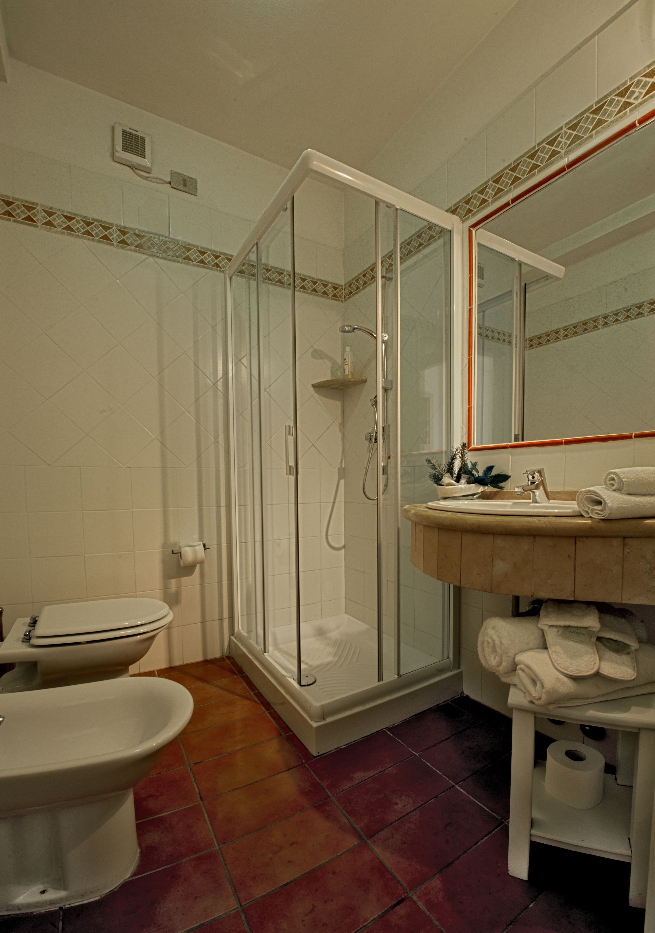 A bathroom with a glass-enclosed shower, a toilet, and a sink with a mirror above it.