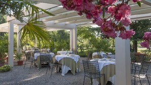 An outdoor patio with tables and chairs, surrounded by greenery and a white pergola. - Villa Belfiore (Ostellato)