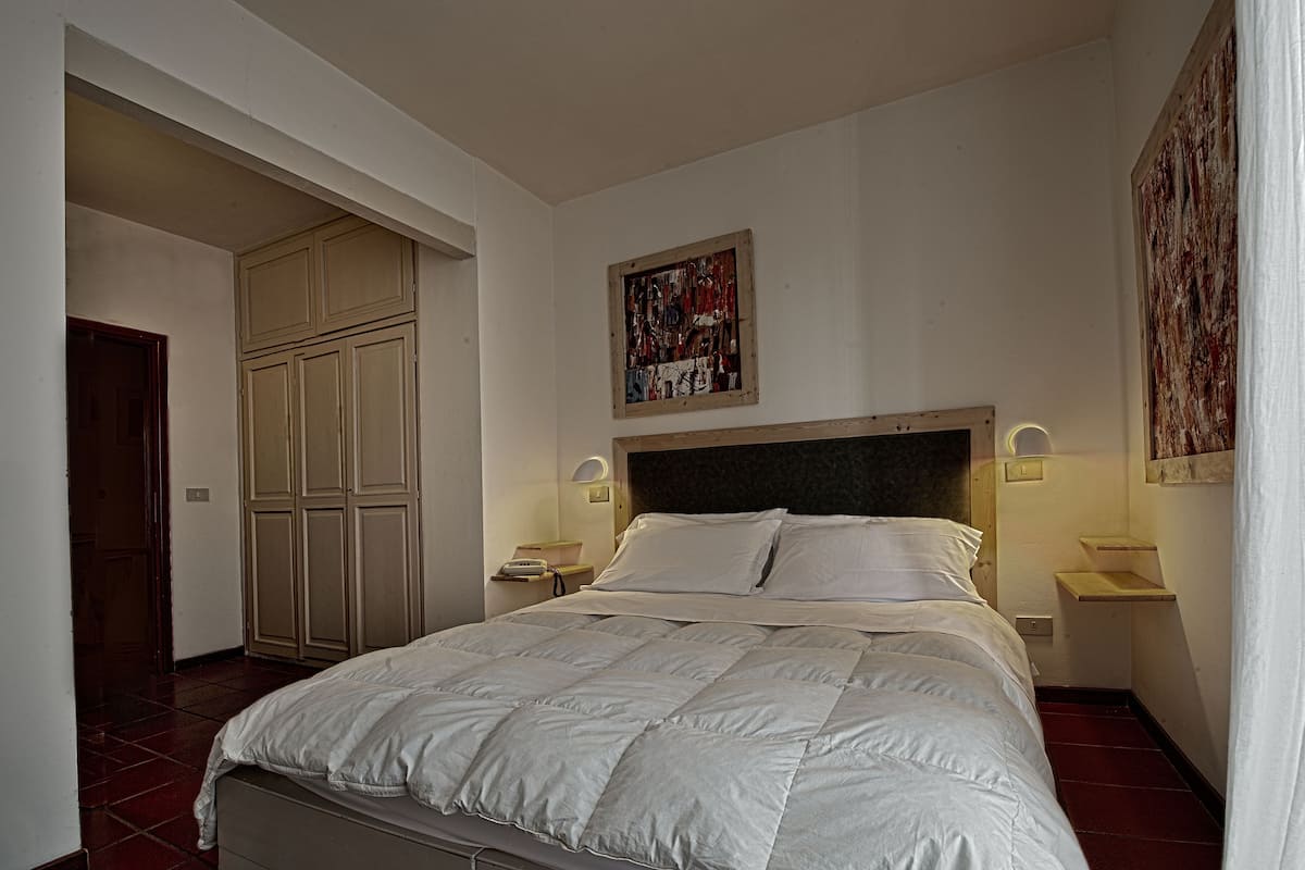 A bedroom with a bed, a wardrobe, a painting, and bedside lamps.