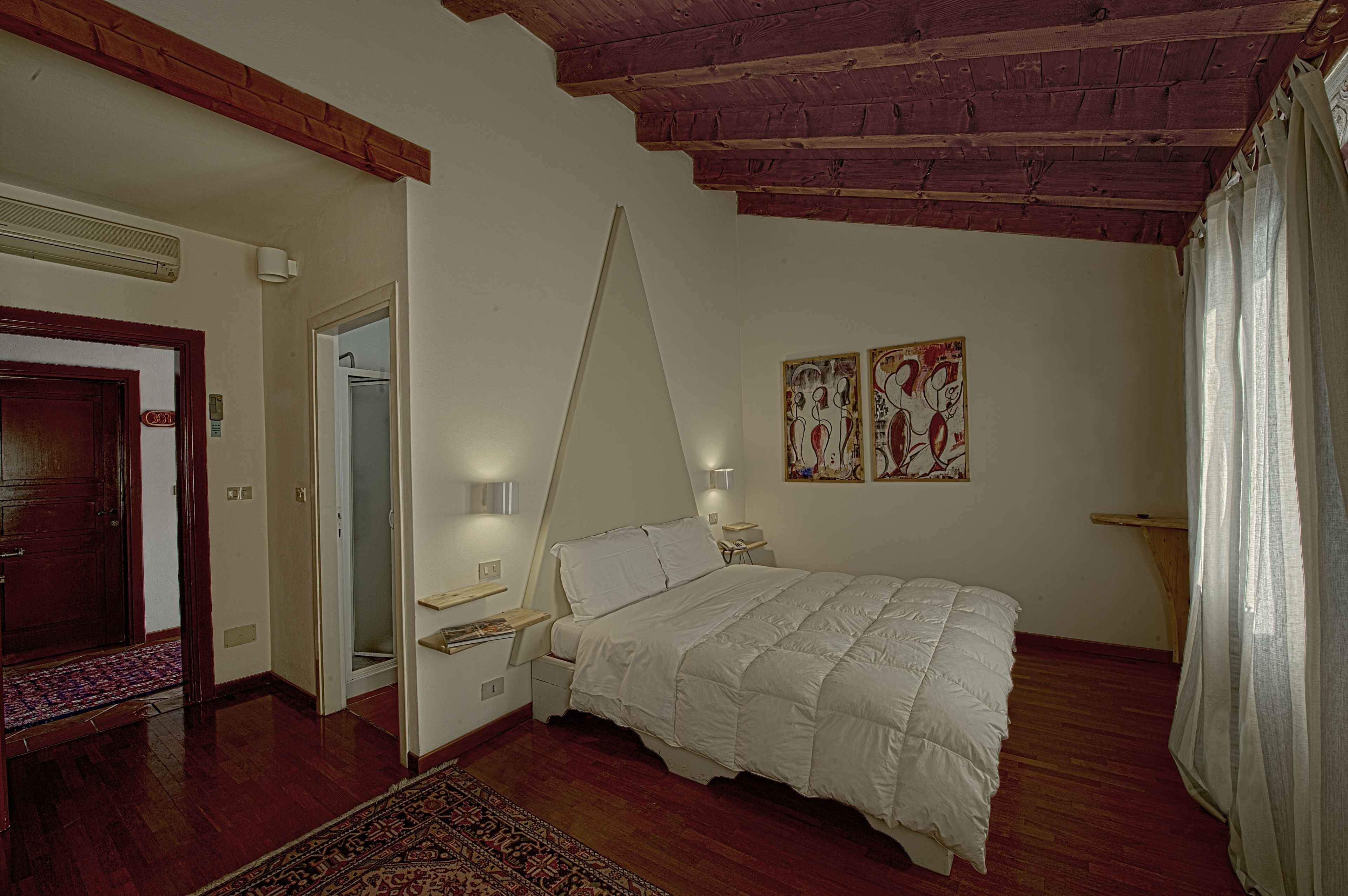 A bedroom with a bed, nightstands, a wooden ceiling, a door, and a wall with two artworks.
