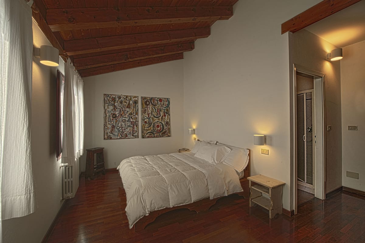 A bedroom with a wooden ceiling, a bed, two wall-mounted lamps, and artwork on the wall.