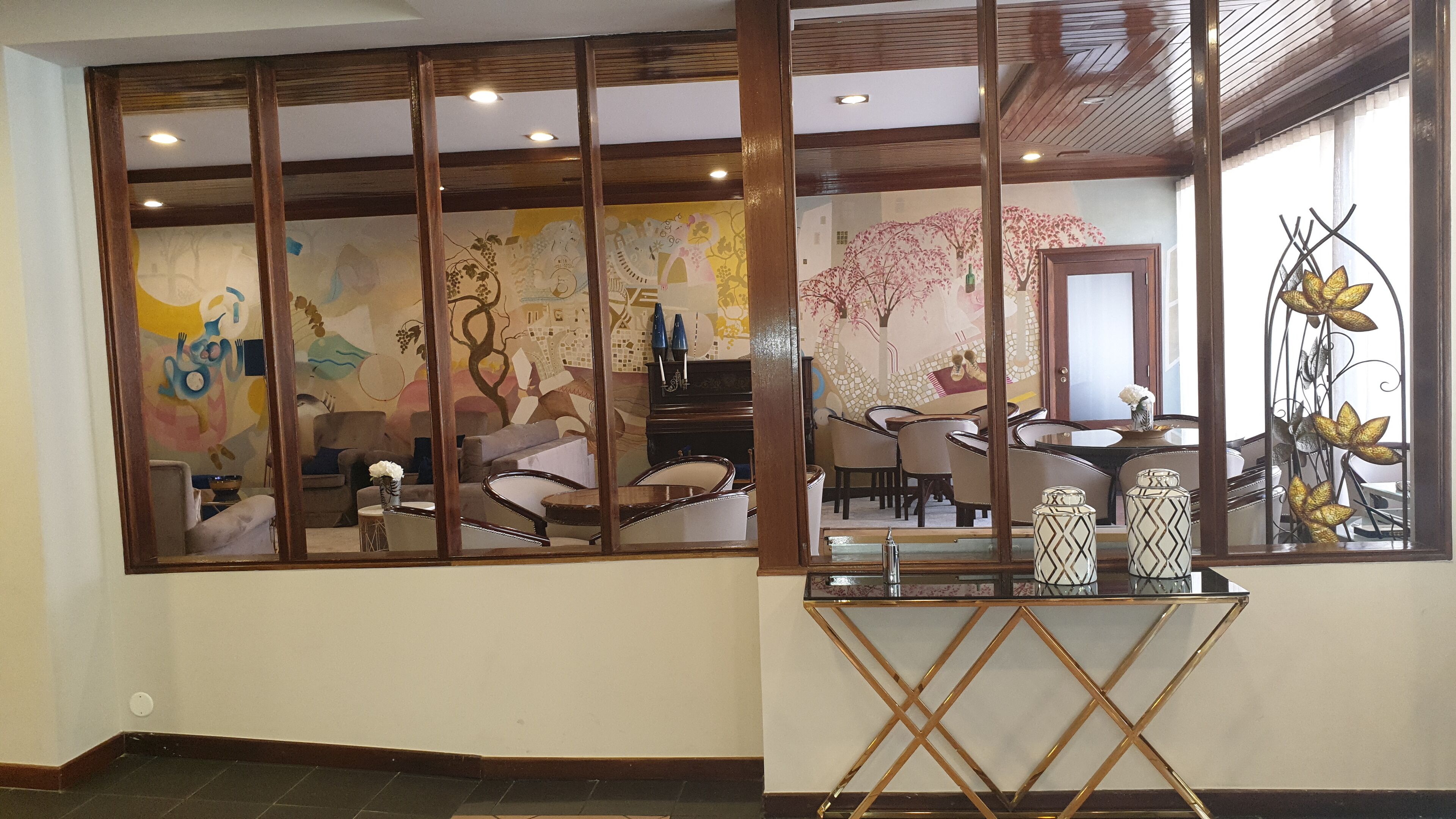 Una habitación con un ventanal grande, un comedor con sillas y una mesa, y un espejo decorativo con motivos florales.