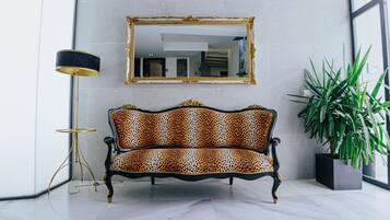 Ein Sofa mit Leopardenmuster, ein Spiegel mit goldener Rahmung darüber und eine Stehlampe links.