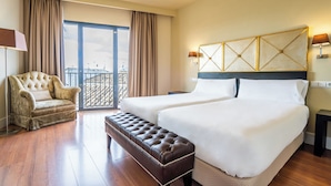 Habitación de hotel con dos camas, un sofá, un banco y vista a la ciudad.