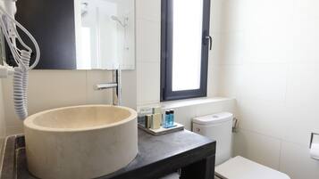 Un baño moderno con un lavamanos grande y redondo, un inodoro y un espejo sobre el lavamanos.