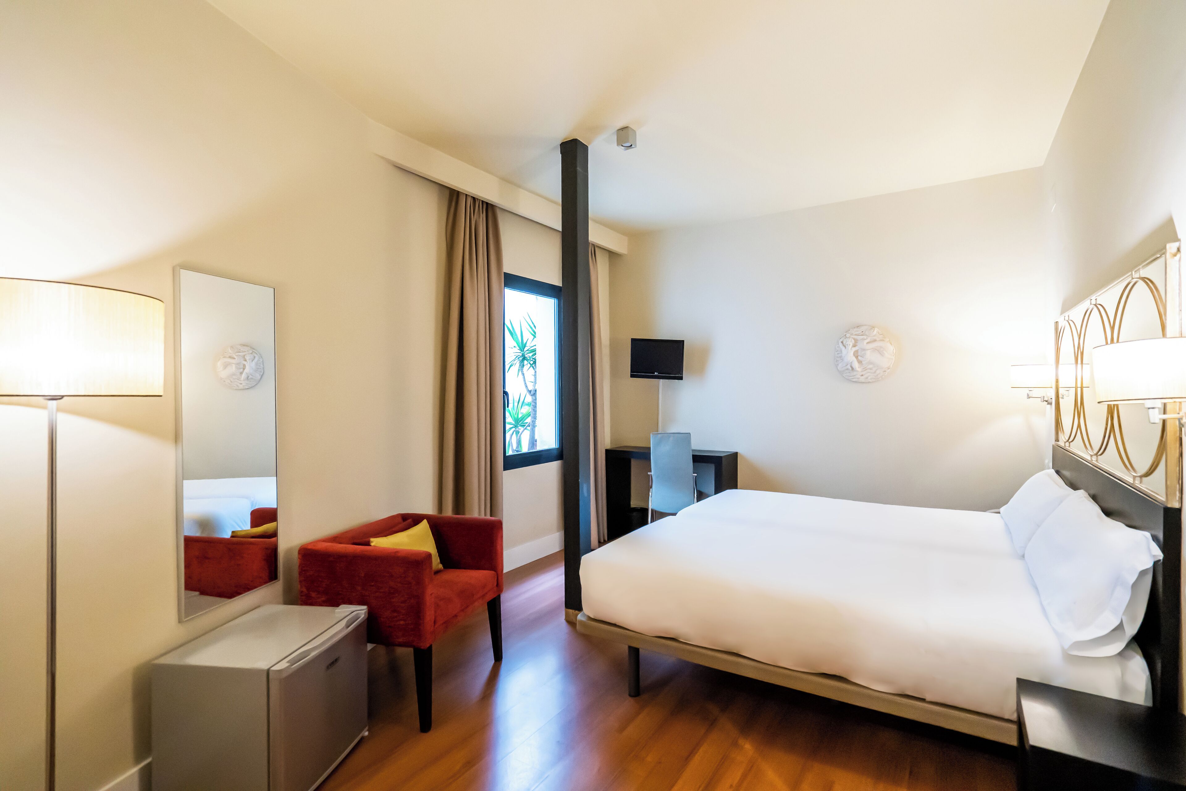 Een hotelkamer met een bed, bureau, stoel, spiegel en televisie.
