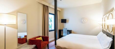 A hotel room with a bed, a desk, a chair, a mirror, and a TV.