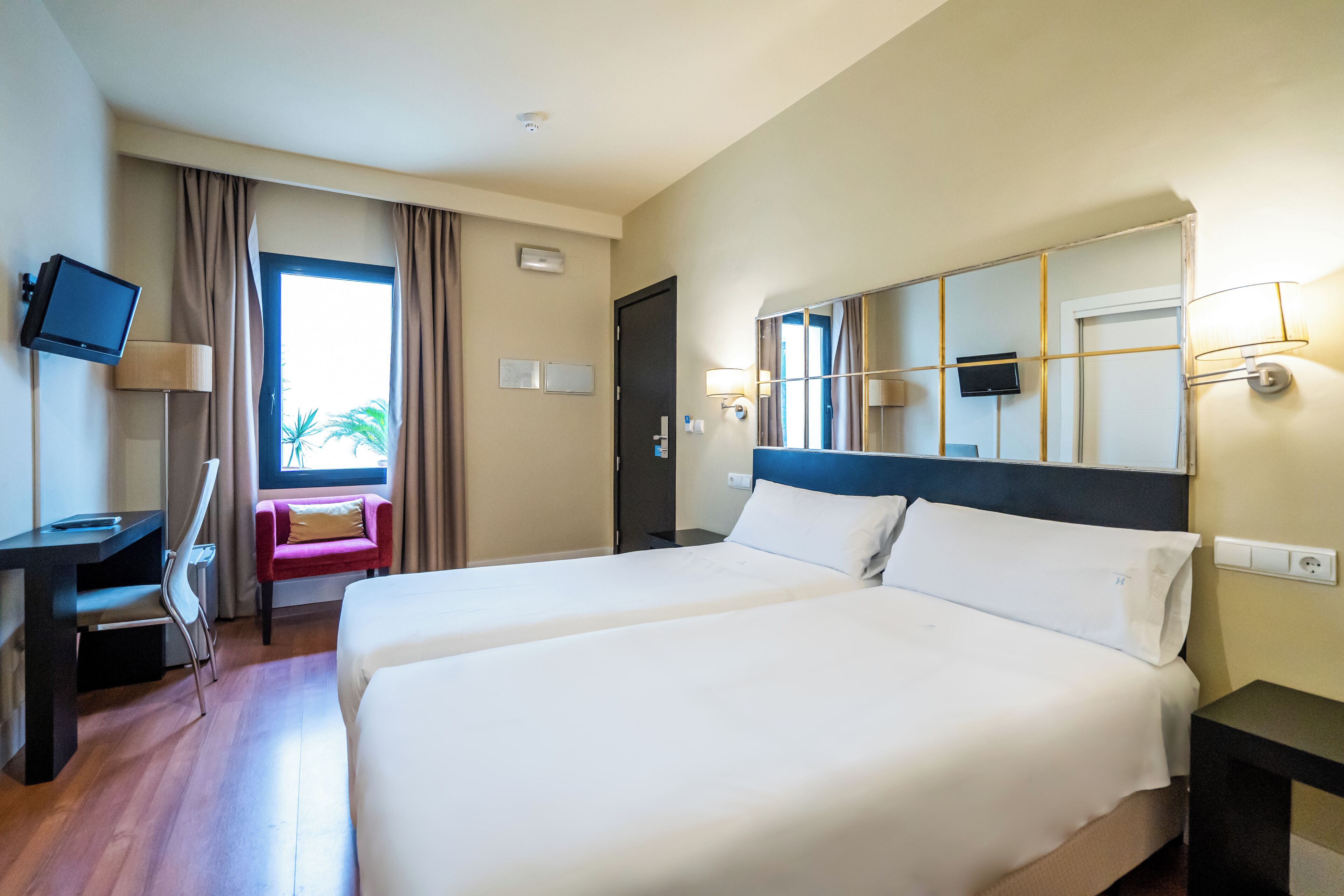 Habitación de hotel con dos camas, un escritorio, una silla, un televisor y una ventana con cortinas.