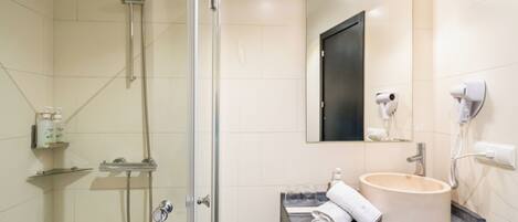 A modern bathroom with a glass-enclosed shower, a sink with a mirror above, and a hairdryer on the wall.