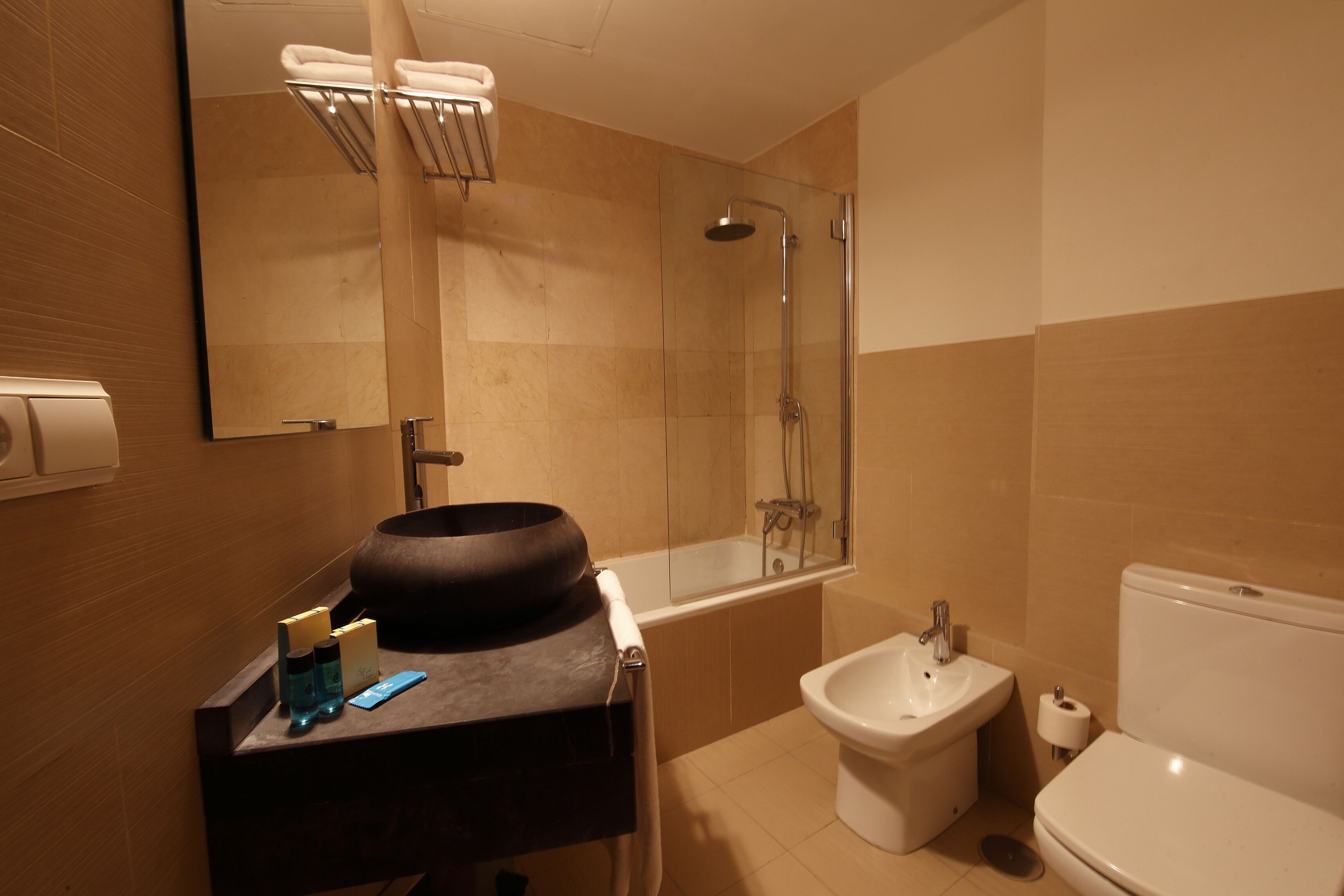 Un baño moderno con un espejo grande, un lavabo redondo, un bidé, una bañera y un inodoro.