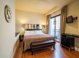 Una habitación de hotel con una cama grande, un banco, un televisor y un balcón con cortinas.