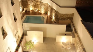 Un área de piscina en la azotea con muros de piedra, mobiliario exterior blanco y un pequeño jardín.