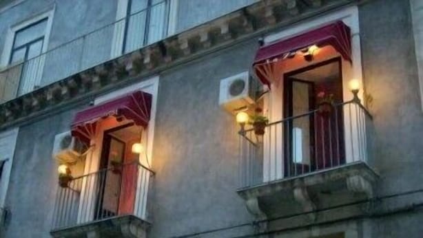 Un edificio con due balconi, ciascuno con un tendalino rosso e un piccolo fiorino.