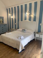 Quarto com uma cama grande, duas mesas de cabeceira, um penteou e uma parede com listras verticais.