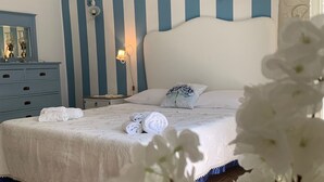 Camera da letto con parete a righe blu e bianche, un letto con biancheria da letto bianca e un comò con uno specchio.