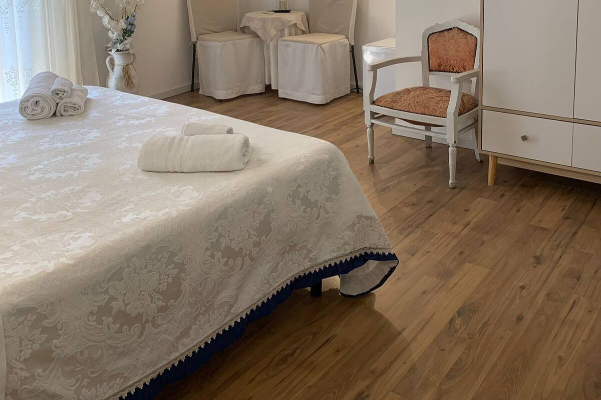 Una camera da letto ordinata con un letto, due sedie, un tavolino, un armadio, una televisione e un condizionatore d'aria a muro.