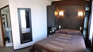 A modern hotel room with a large bed, a built-in wardrobe, a bedside table with a lamp, and a mirror. - Hôtel du Parc Even (Malakoff)