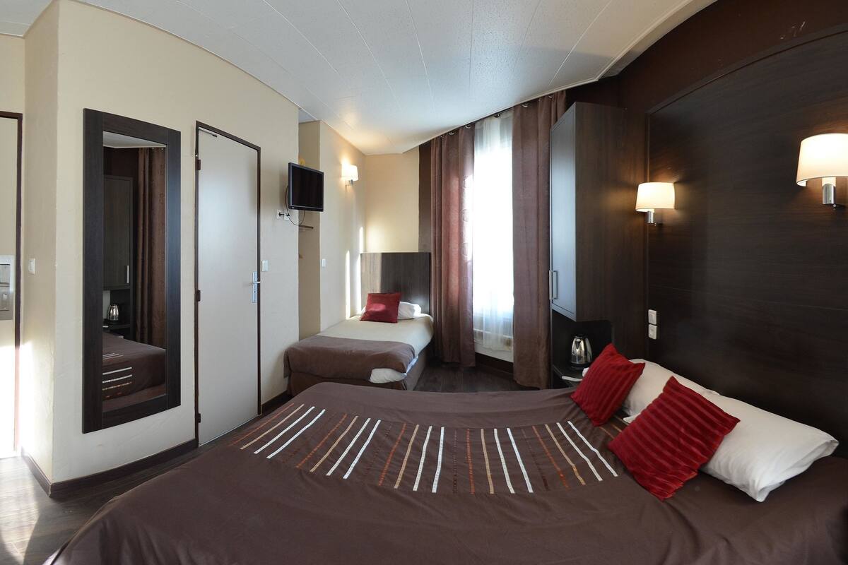 Una habitación de hotel con una cama grande, una cama más pequeña, un televisor y un escritorio con una lámpara.