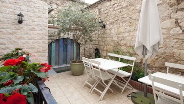 A stone-walled courtyard with a white table and chairs, a potted plant with red flowers, and a white umbrella. - Hôtel du Parc Even (Malakoff)
