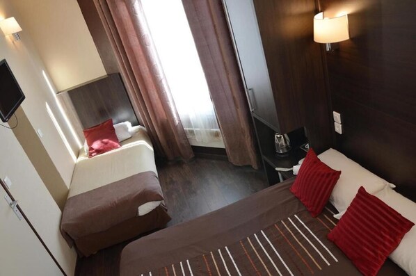 A hotel room with two beds, a TV, a bedside table, and a window with curtains. - Hôtel du Parc Even (Malakoff)