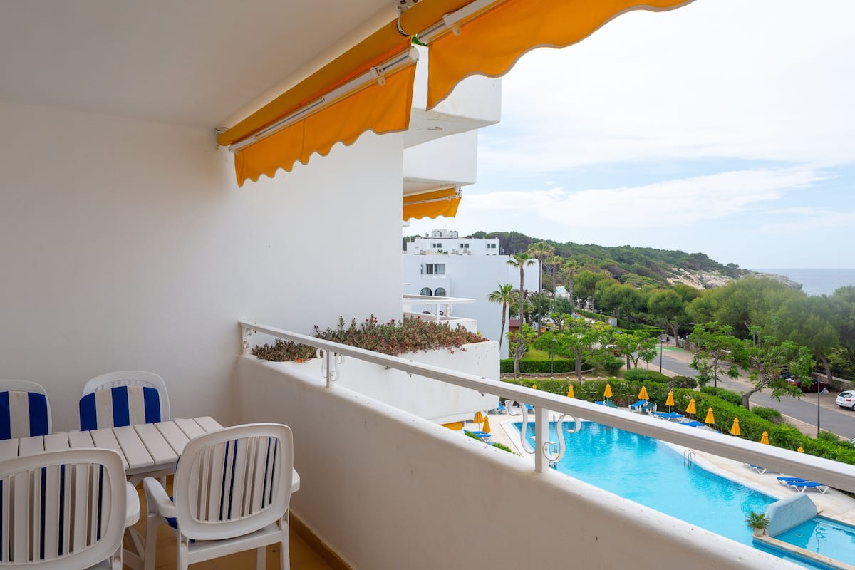 Ein Balkon mit Blick auf einen Pool, weißen Stühlen und einem gelben Sonnenschirm.