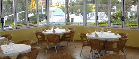 A restaurant with multiple tables and wicker chairs, large windows with decorative borders, and a view of the outside.
