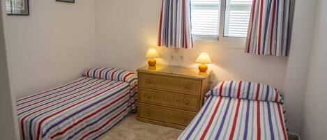 Une chambre avec deux lits simples, une commode et deux lampes de chevet.