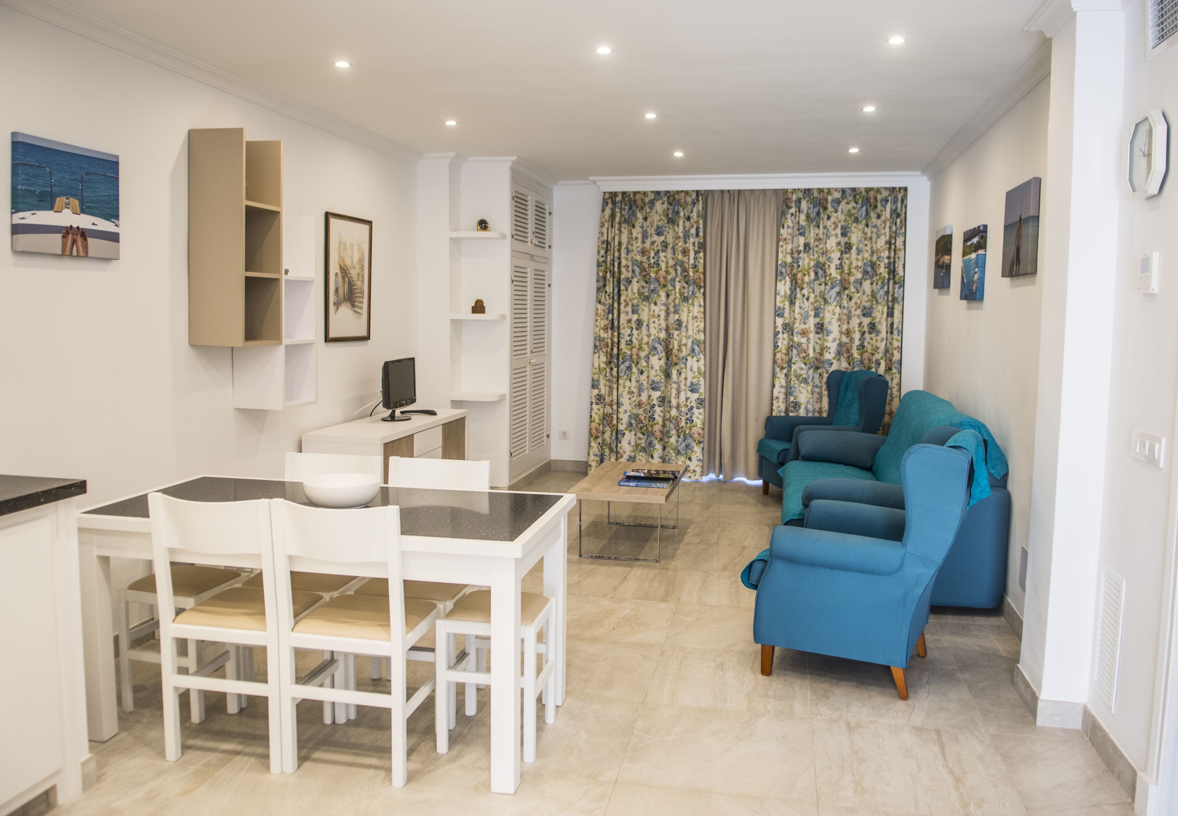 Una sala de estar moderna con un sofá, una mesa de comedor con sillas y una cocina con armarios y un refrigerador.
