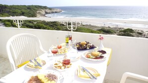 A table set with various dishes and drinks on a balcony overlooking a beach. - Hamilton Court  Apartamentos (Es Migjorn Gran)