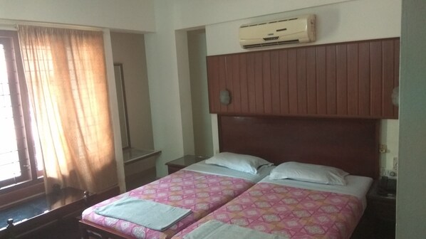 Habitación de hotel con dos camas, cabecera de madera, aire acondicionado, un espejo y una ventana con cortinas.