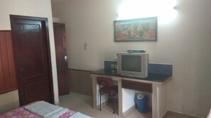 Una habitación con cama, un escritorio con televisor, una silla y un cubo de basura.