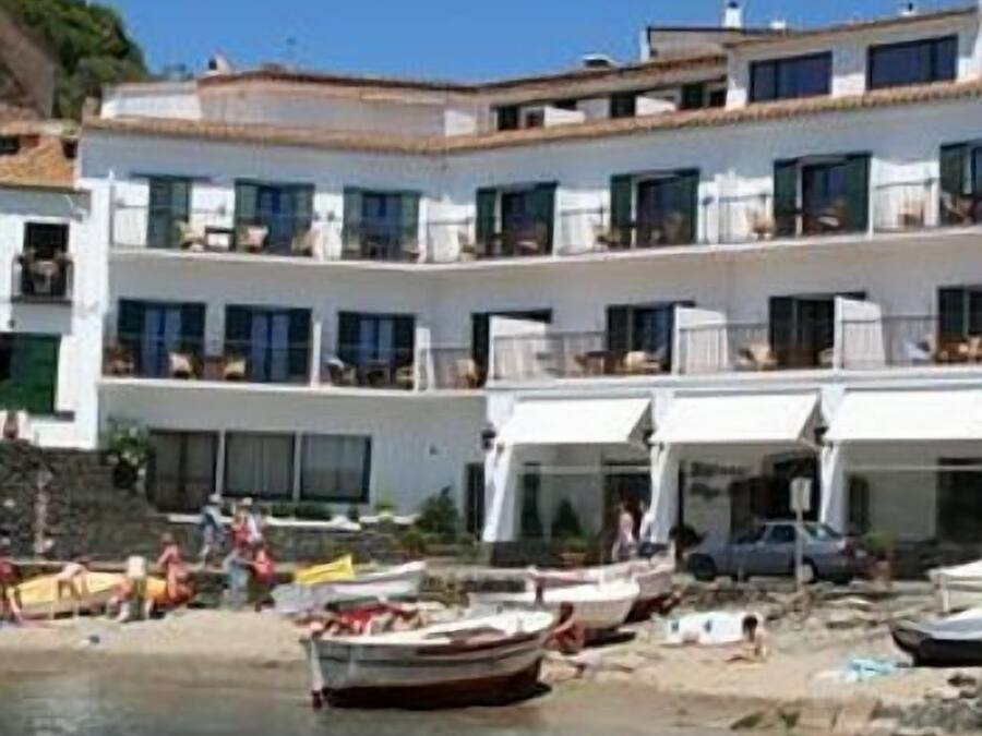 Un edificio de varios pisos con balcones, una playa en primer plano y embarcaciones.