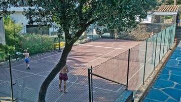 An outdoor tennis court with a net, surrounded by a fence and trees.