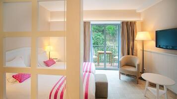 A hotel room with a balcony, a television, a chair, and a bed with a striped bedspread.