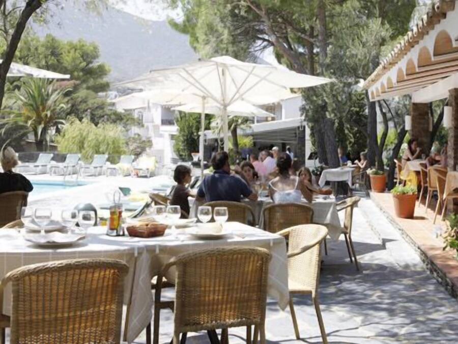 Un espacio de comedor al aire libre con mesas y sillas, una piscina y sombrillas.