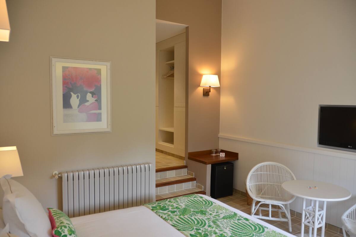 A hotel room with a bed, a small table, two chairs, a TV, a painting, and a staircase leading to a closet.
